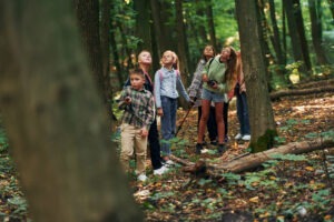 With touristic equipment. Kids in green forest at summer daytime together.